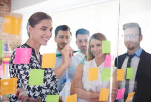 Office workers writing with dry erase markers and sticky notes on glass